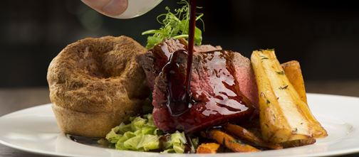 Gravy being poured over roast sirloin of Welsh beef, roasted root vegetables and Yorkshire pudding,
