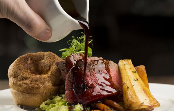Gravy being poured over roast sirloin of Welsh beef, roasted root vegetables and Yorkshire pudding,