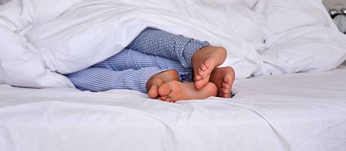 Couples feet sticking out of duvet at the end of the bed