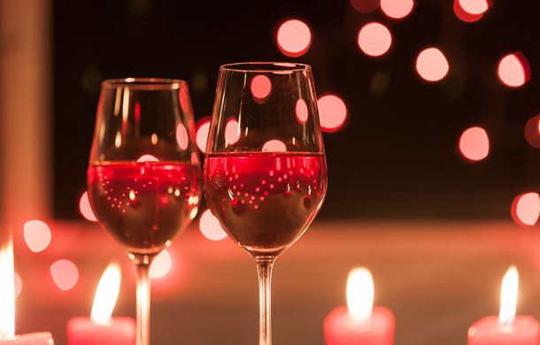Two wine glasses with candles in background 