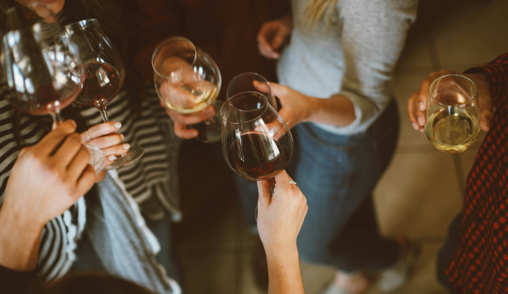 Five people standing and holding wine glasses filled with red and white wine, viewed from above.