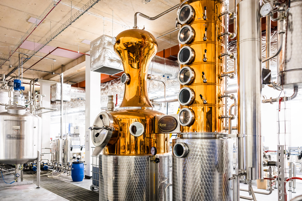Copper and steel distillation columns in a modern distillery, with pipes and tanks in the industrial setting.