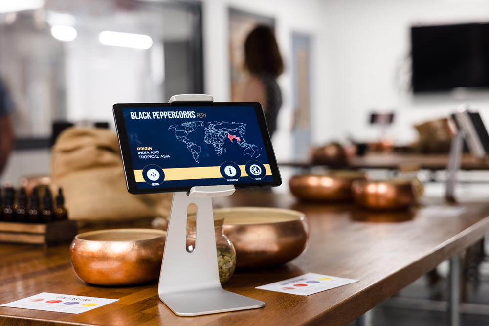 Tablet displaying information about black peppercorns on a wooden table with copper bowls and spice containers.