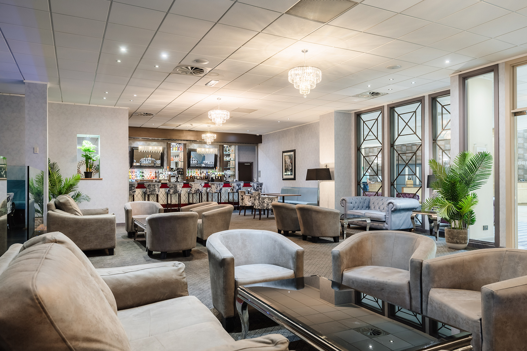 Elegant lounge area with plush seating, a chandelier ceiling, and a well-stocked bar in the background.