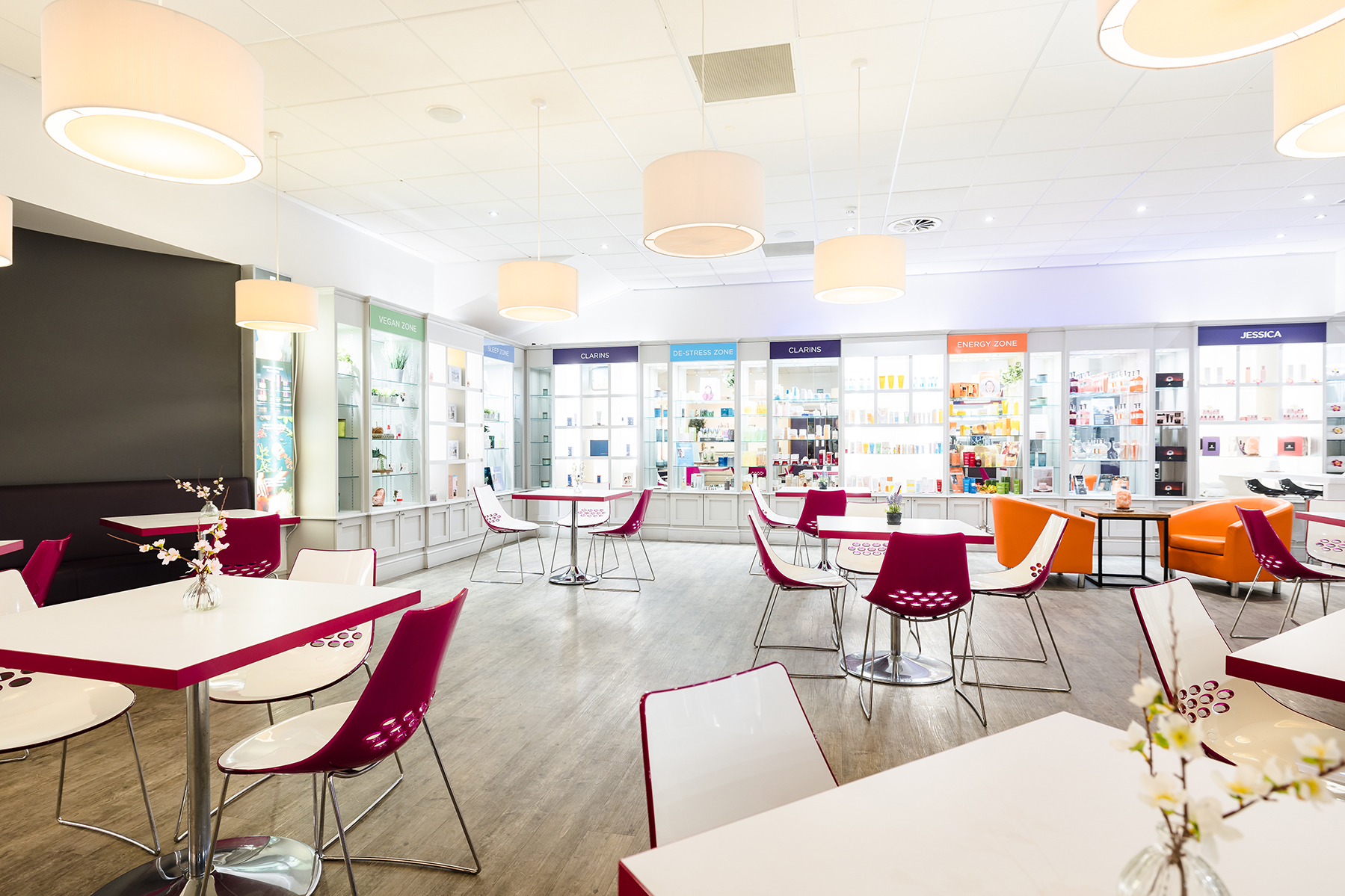 Bright, modern cafe interior with white tables, colorful chairs, and displays of products along the walls.