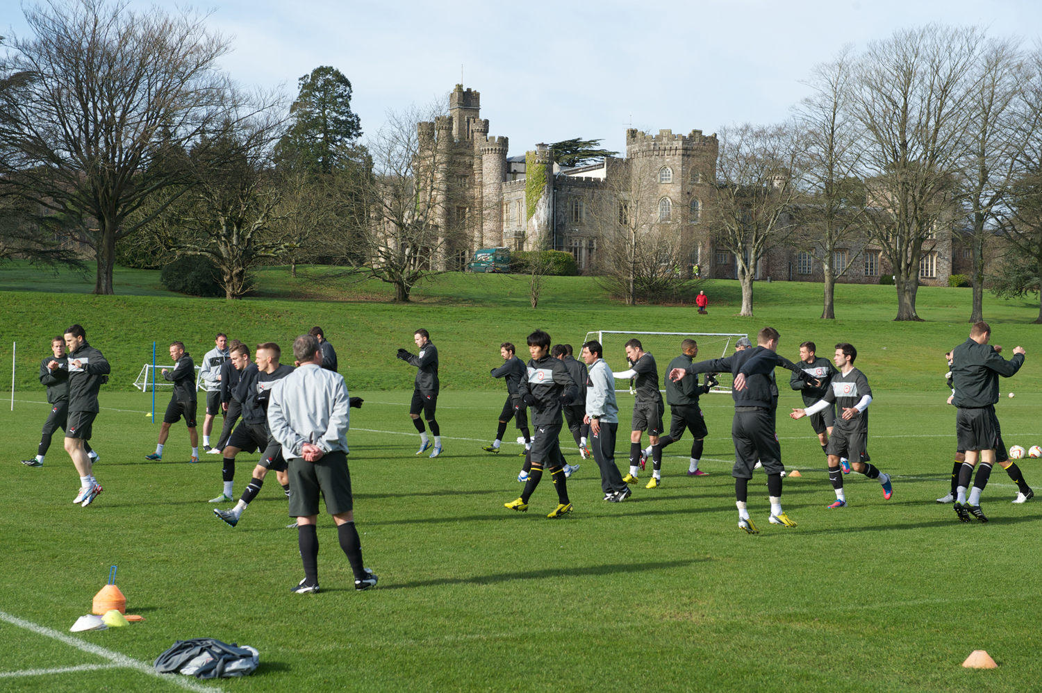 Soccer team practicing on a grassy field in front of a large, historic building on a clear day.