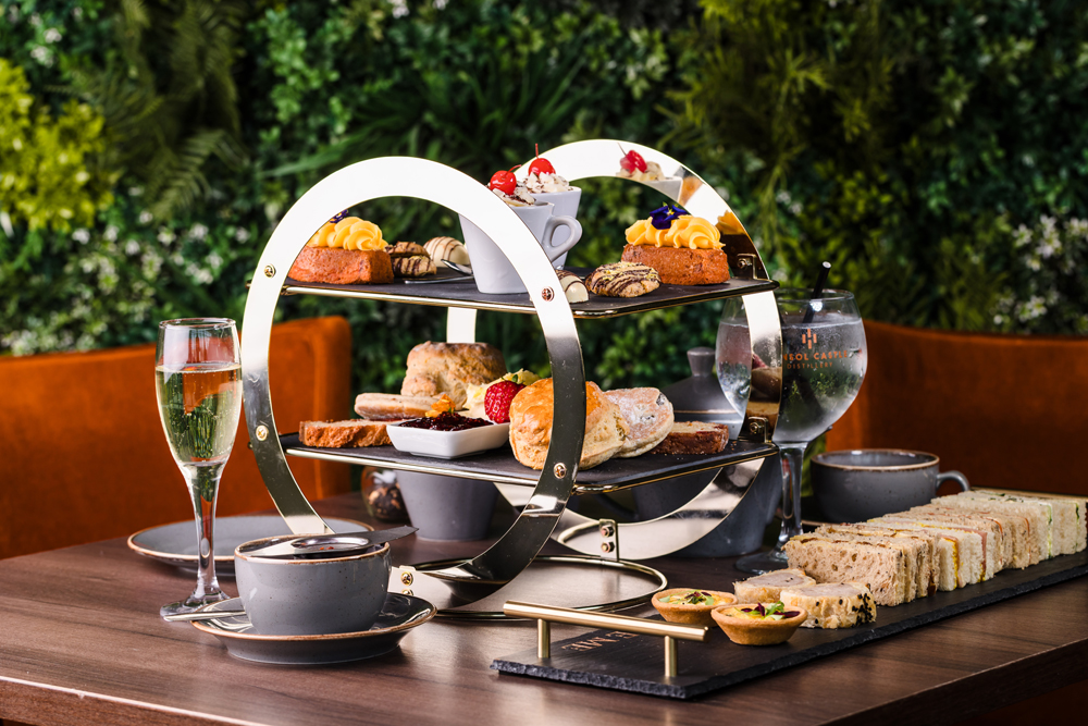 A tiered stand with pastries, scones, and desserts beside tea, champagne, and a platter of assorted finger sandwiches.