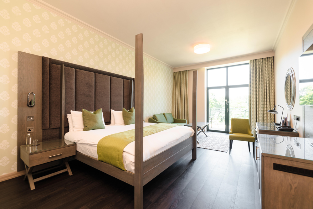 Modern hotel room with a large bed, green accents, a desk, and a window overlooking greenery.