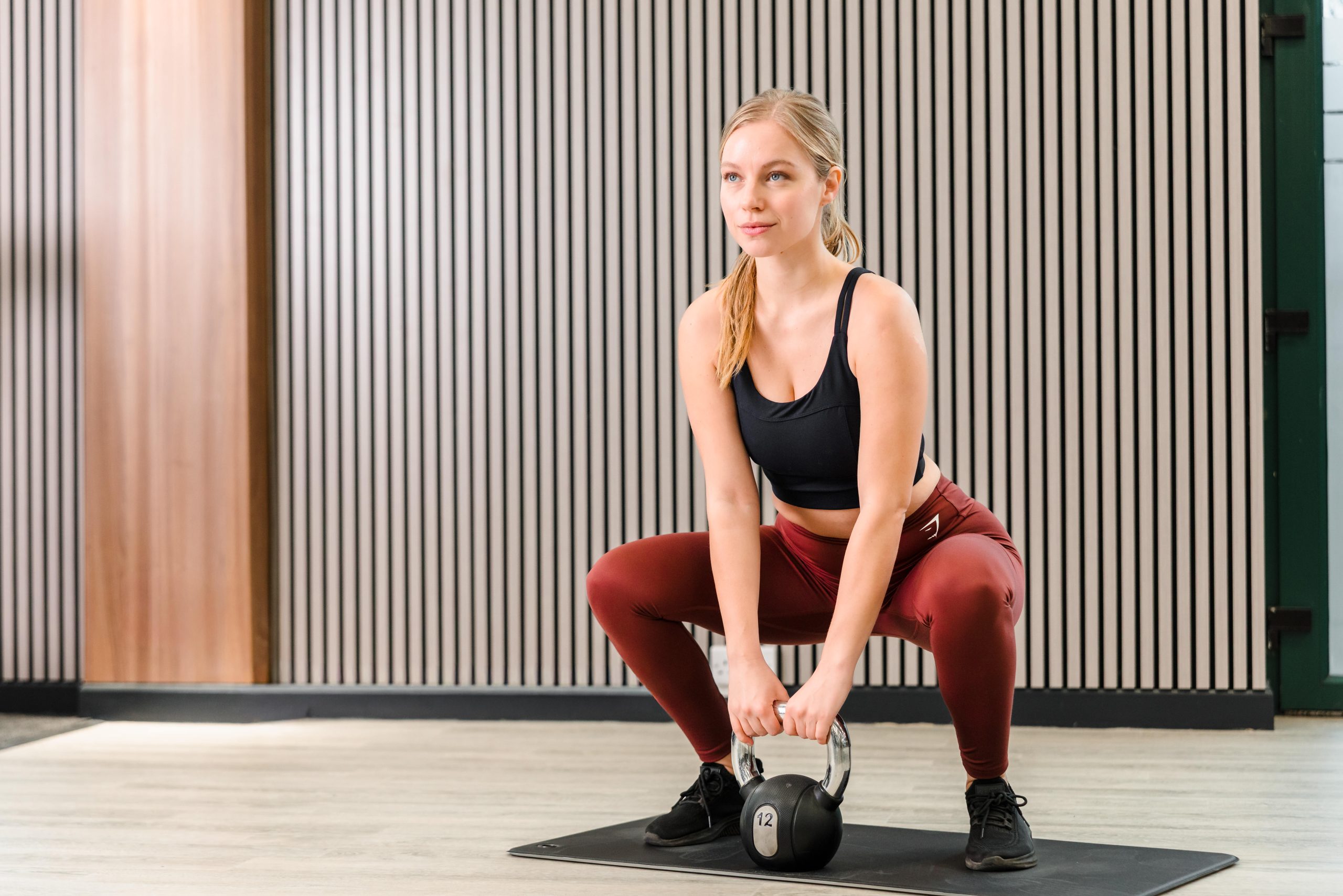 Woman in workout gear doing a kettlebell squat on a mat in the newly refurbished Vale Resort South Wales Gym.
