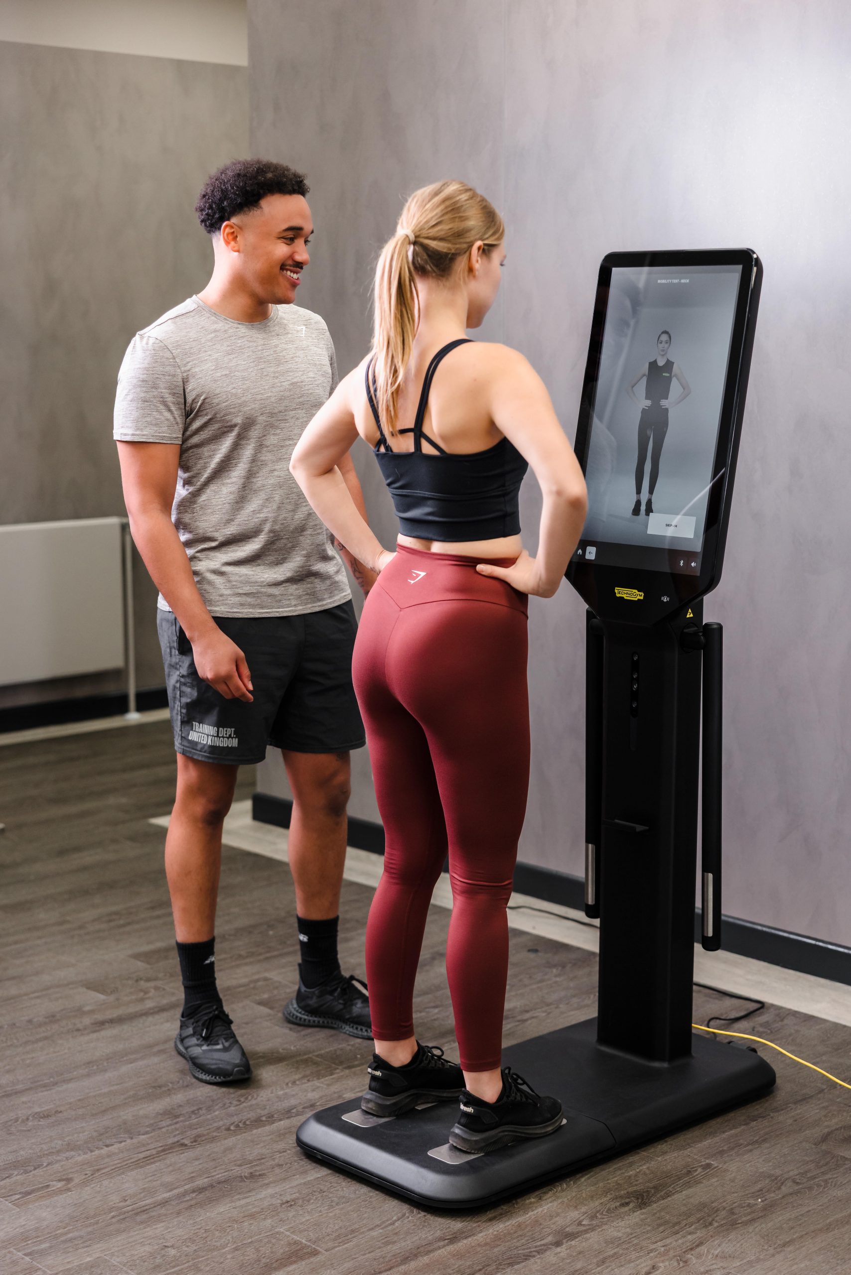 Two people use a fitness mirror showing an exercise guide in the newly refurbished Vale Resort South Wales Gym.