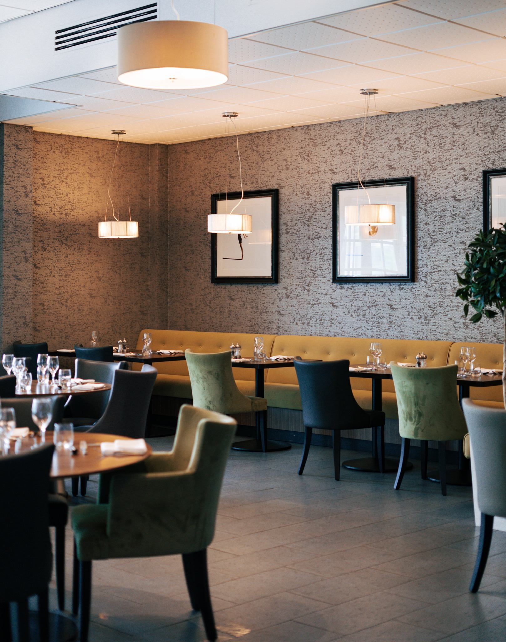 Modern restaurant interior with green and yellow chairs, set tables, wall art, pendant lighting, and vacancies available.