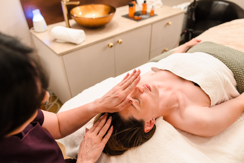 A person receives a facial massage while lying on a treatment table in a spa setting.