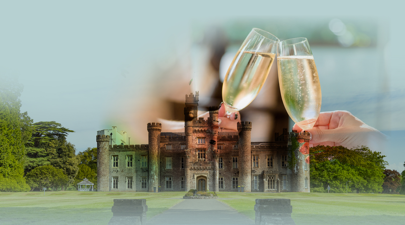 Two people clink champagne glasses in front of a large historic stone castle with a green lawn and trees.