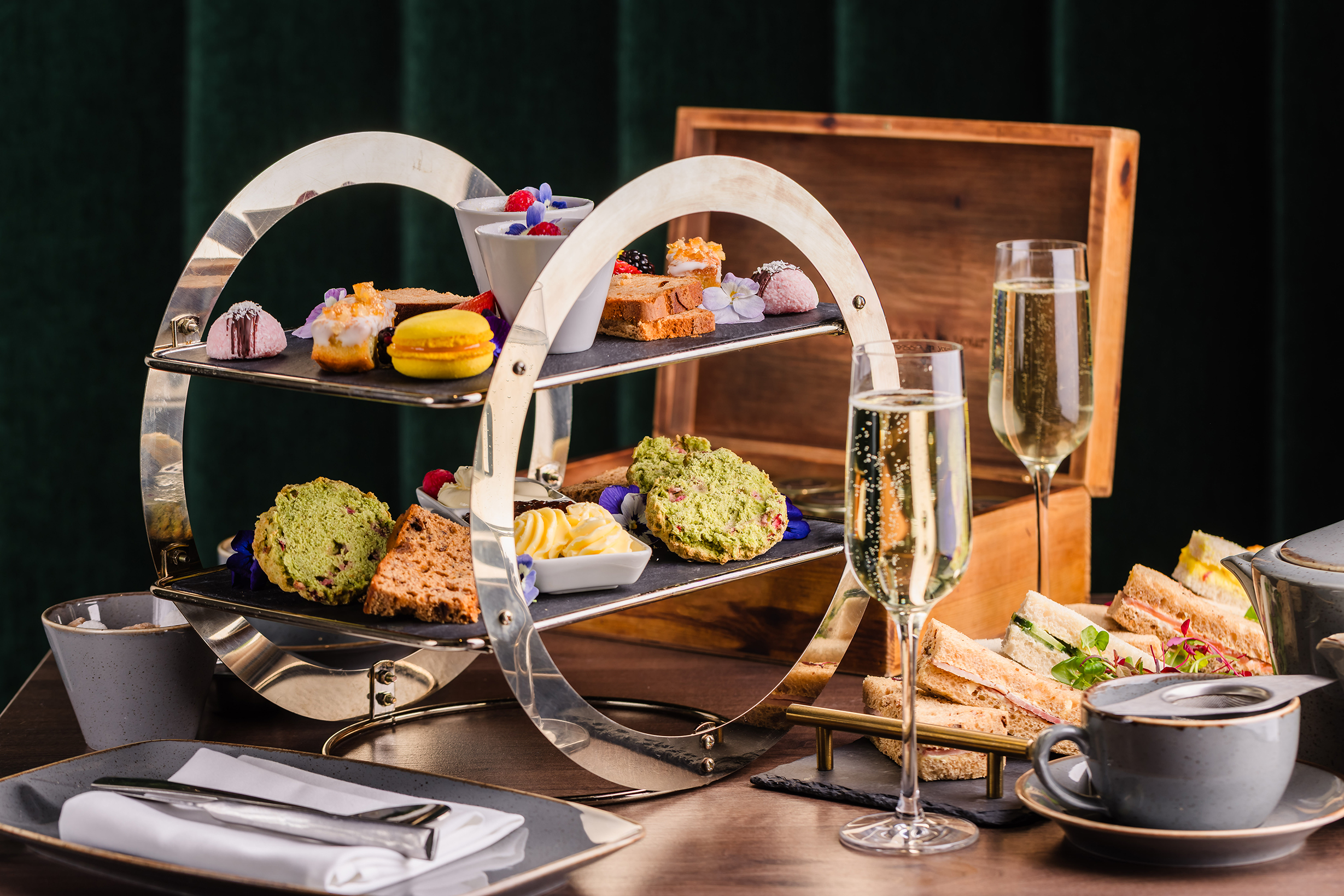 A two-tiered tray with assorted pastries, scones, and sandwiches—perfect for an elegant afternoon tea with sparkling wine.
