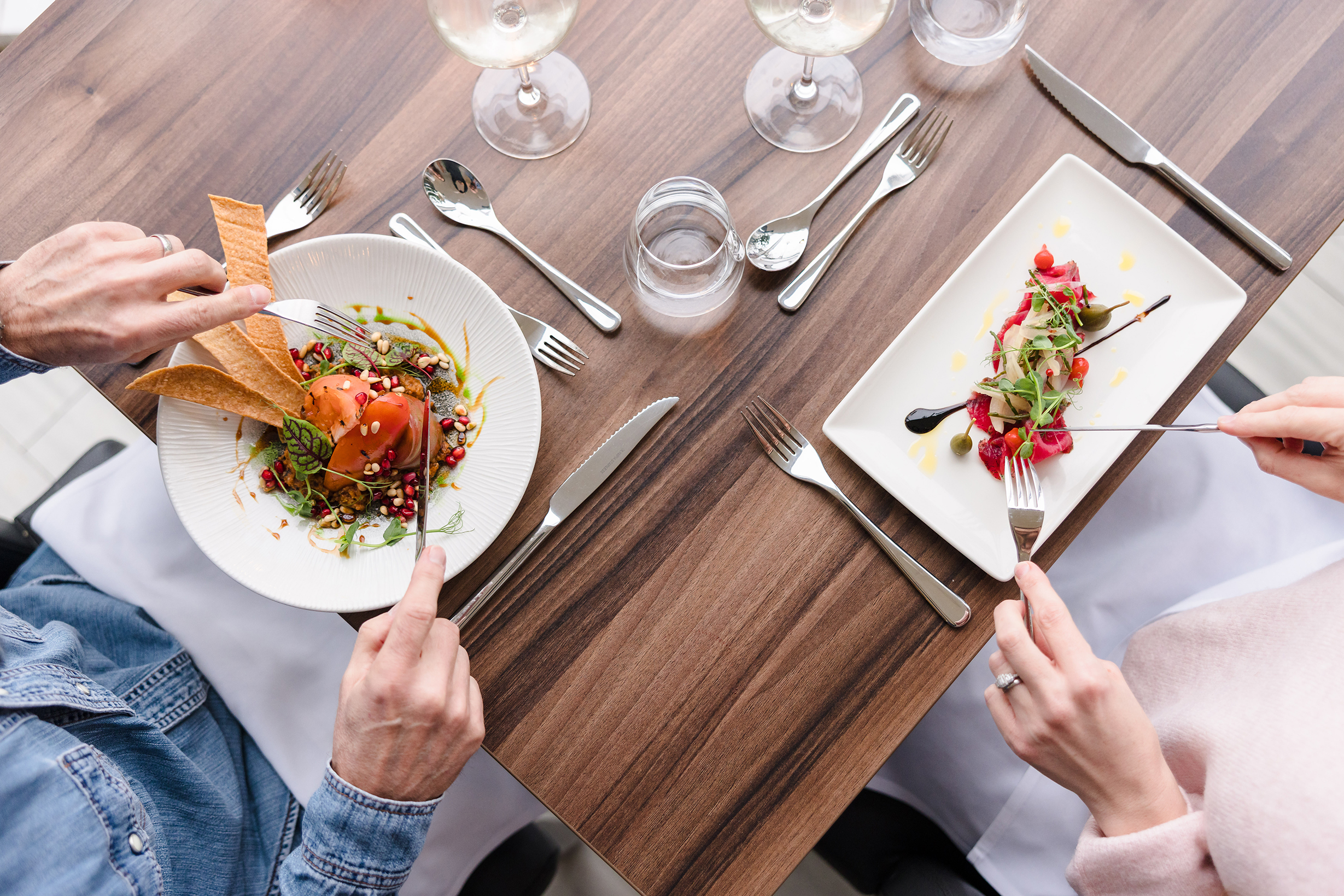Two people enjoying a sunday lunch at a table with gourmet dishes, wine glasses, and neatly arranged cutlery.