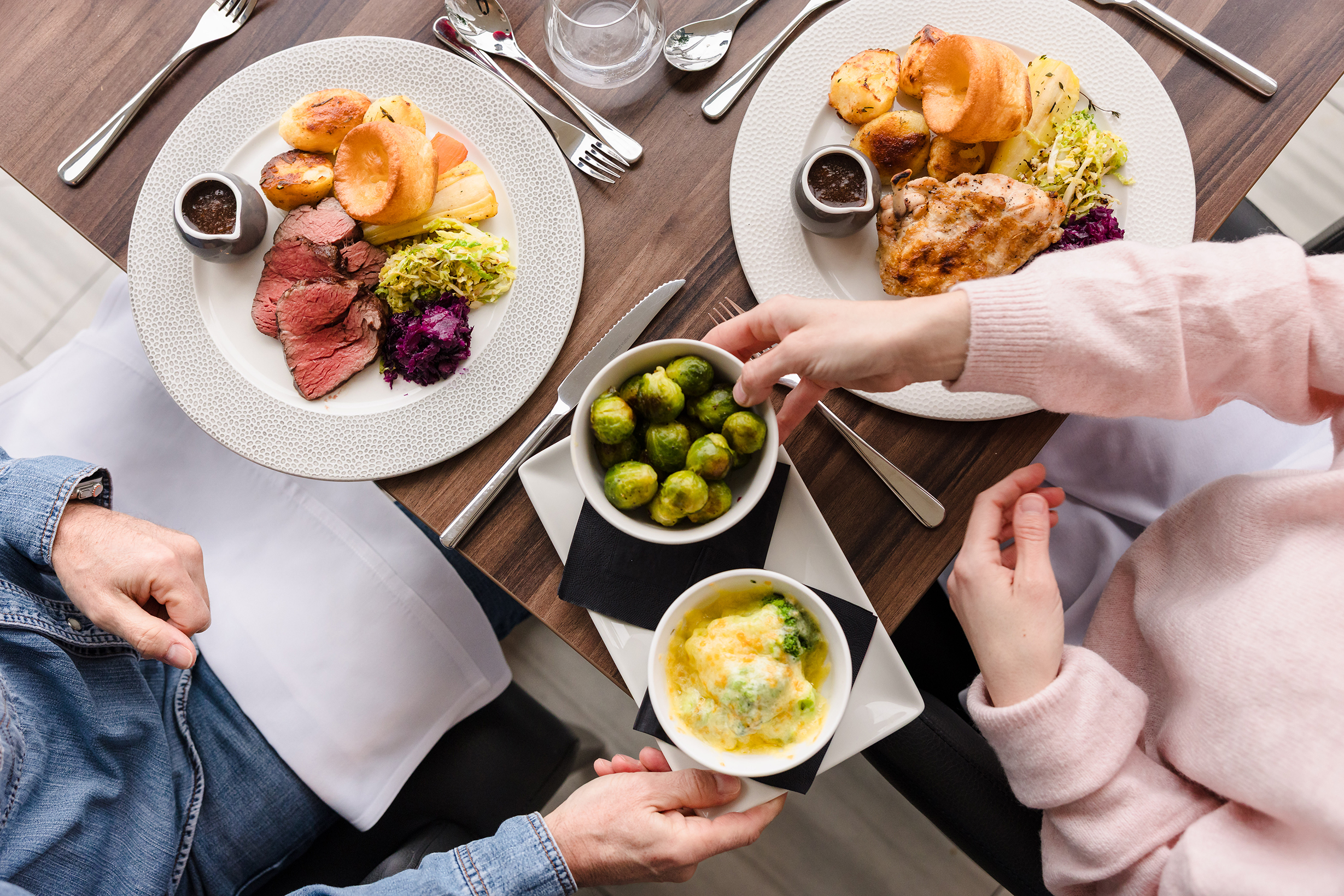 Two people enjoying a hearty Sunday lunch with roast meat, potatoes, vegetables, and shared side dishes.