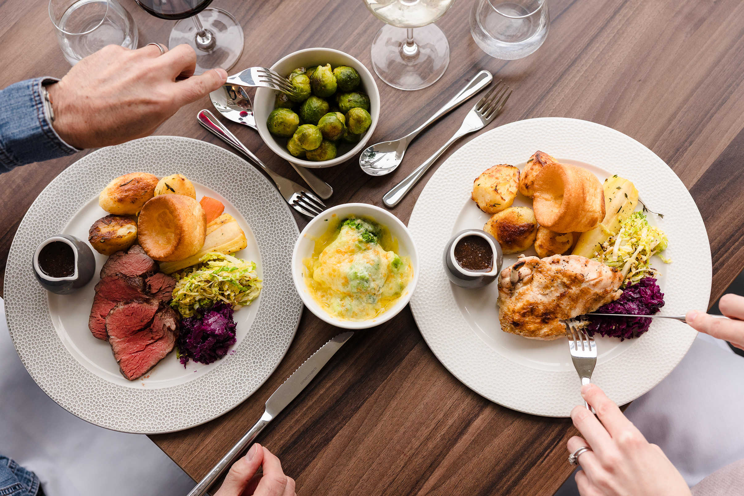 Two plates of roast dinners with vegetables and Yorkshire pudding, perfect for a cozy Sunday lunch on a wooden table.