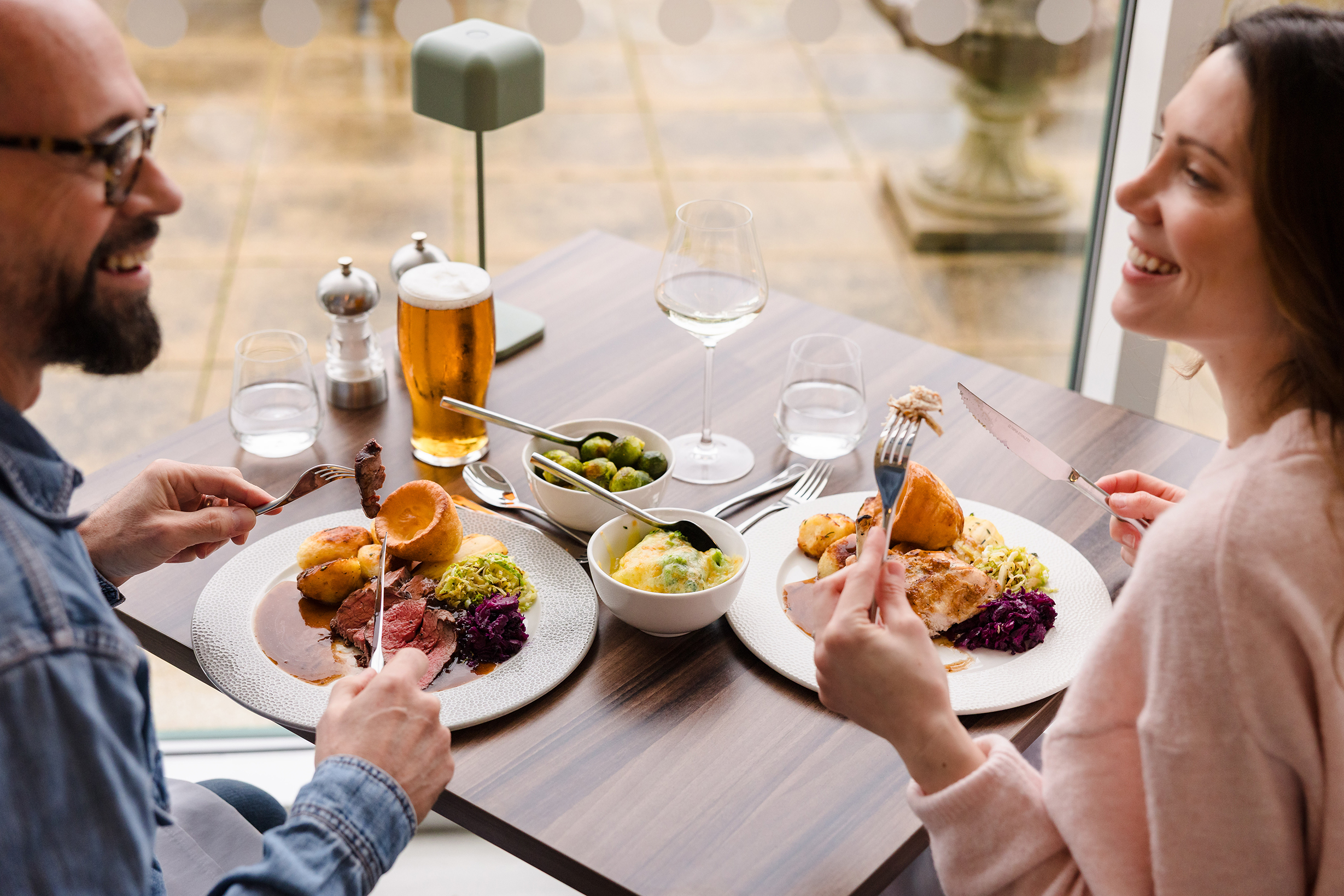 Two people enjoy sunday lunch and drinks, sharing conversation in a bright, modern restaurant setting.