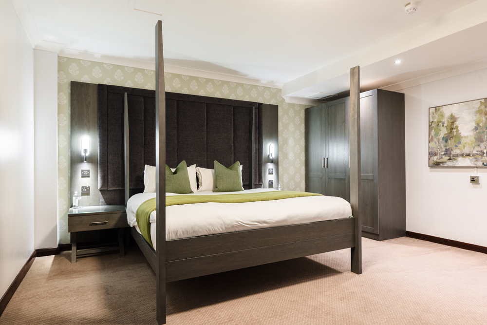 Modern luxury hotel room with a four-poster bed, green accents, bedside tables, wardrobe, and stylish wall art.