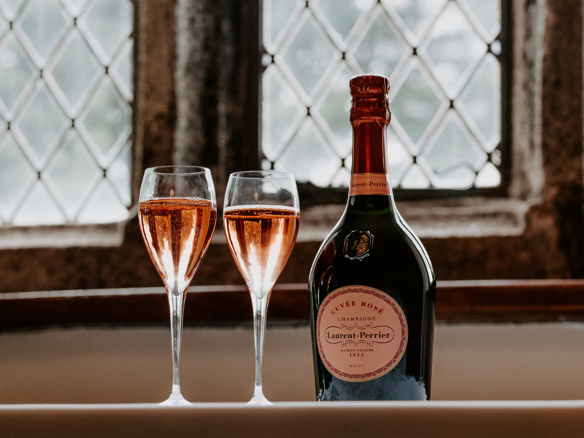 A bottle of Laurent-Perrier Cuvée Rosé champagne with two filled champagne flutes on a windowsill.